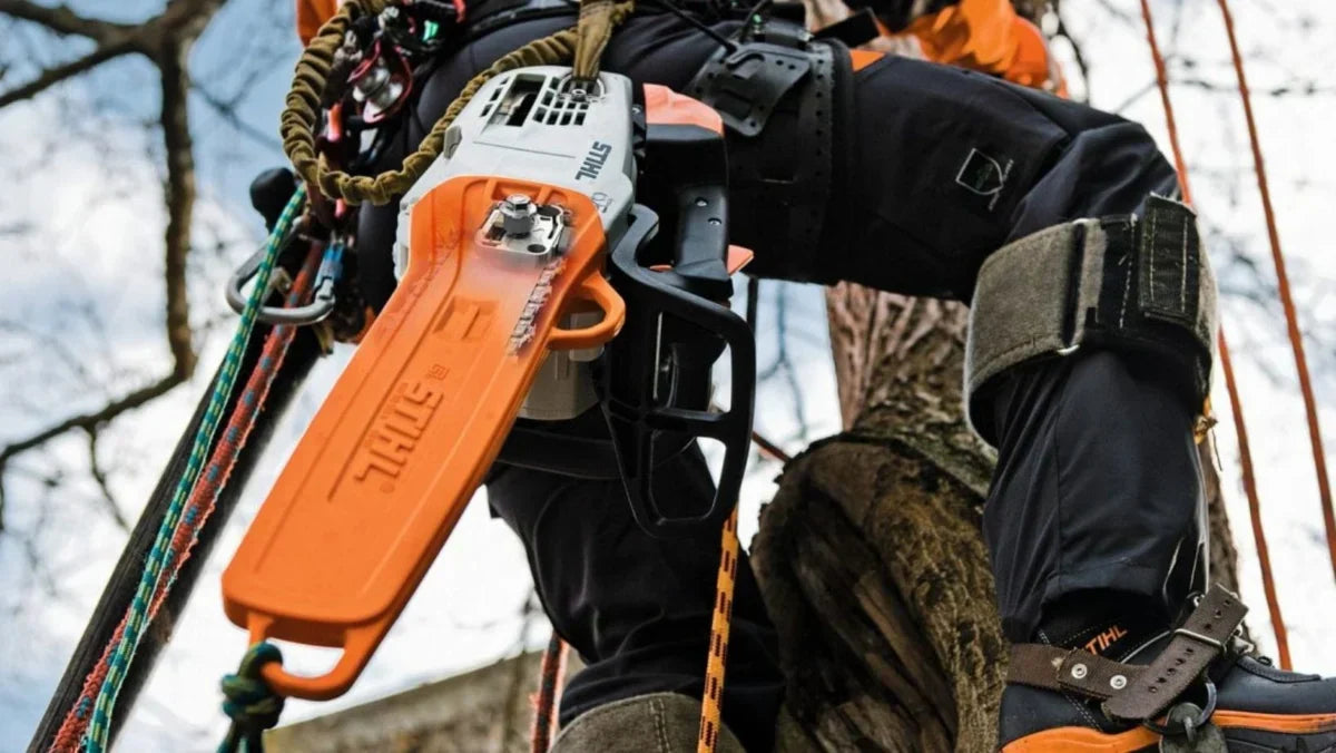 Stihl chainsaw hanging on a harness worn by a man climbing a tree