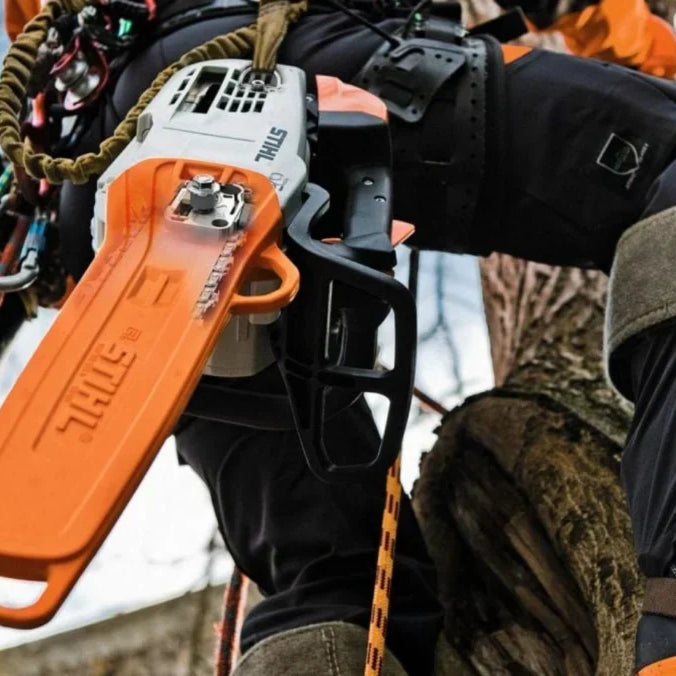 Stihl chainsaw hanging on a harness worn by a man climbing a tree