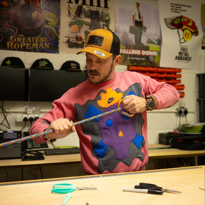 Man in colorful sweater and cap holding a rope in a workshop setting
