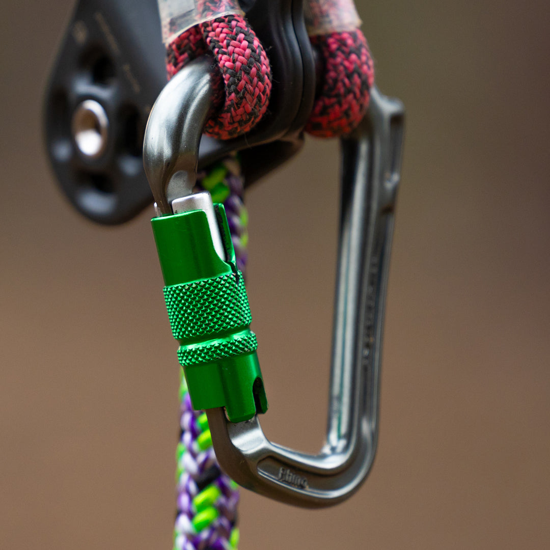 Close-up of a carabiner with a green lock mechanism attached to a rope on a blurred background.